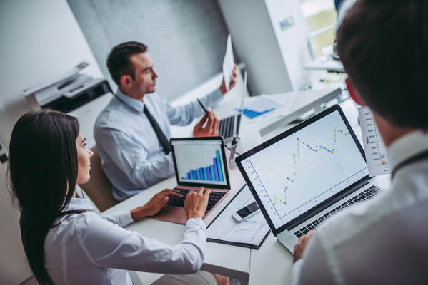 Três pessoas olhando para gráficos em notebooks e folhas