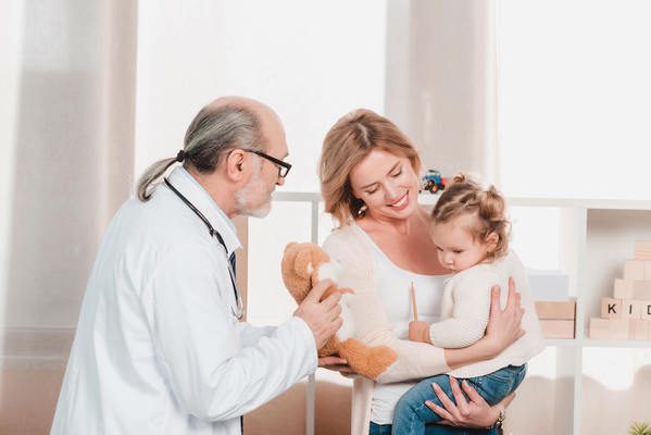 Médico com um urso olhando para uma criança no colo da mãe